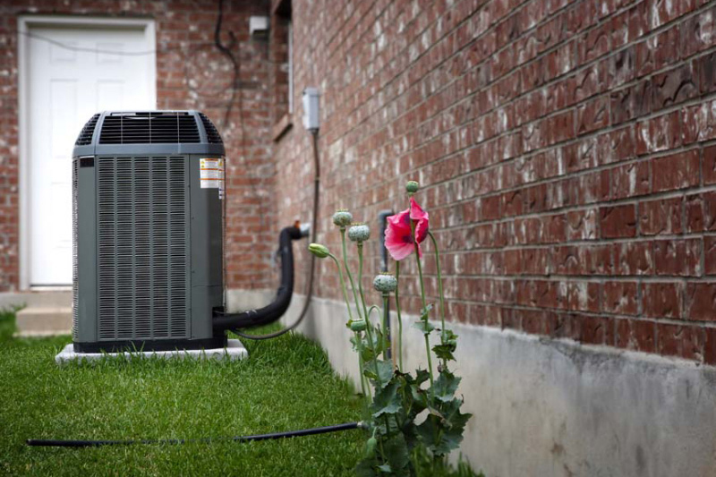 Blog Title How Does an Air Conditioner Work? Photo of Outdoor AC Unit with pink flower and brick home