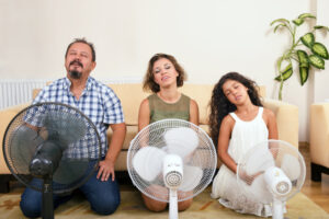 Family sitting on floor of their living room using fans to cool down.