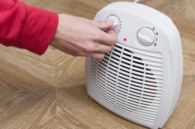 A person adjusts a heater. How to Lower Your Winter Heating Bill.