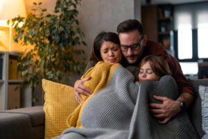 Why Isn’t My Furnace Heating My Entire Home? Mother, father and young daughter are huddled up under covers in their living room trying stay warm.