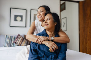 The love between a mother and daughter is forever: a smiling Asian female embracing her mother while they are looking away.