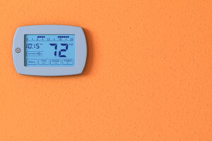 Thermostats 101. One orange wall with a digital thermostat panel.