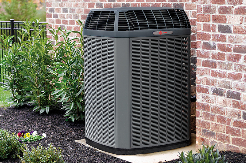 What’s That Smell Coming From My AC at Startup? Photo of an HVAC unit installed outside of a brick home or building.